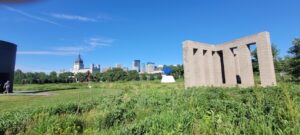 To the left is "Black Vessel for a Saint" by Theaster Gates, with the Basilica of Saint Mary in the background. The sculpture with the blue rooster is "Hahn/Cock" by Katharina Fritsch. The brick structure on the right is x with columns by sol lewitt